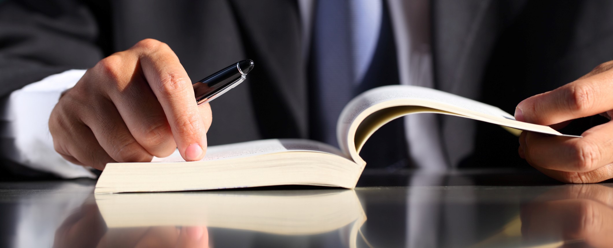 Businessman with Pen and Book Close-up of businessman holding pen with opened book at desk.
